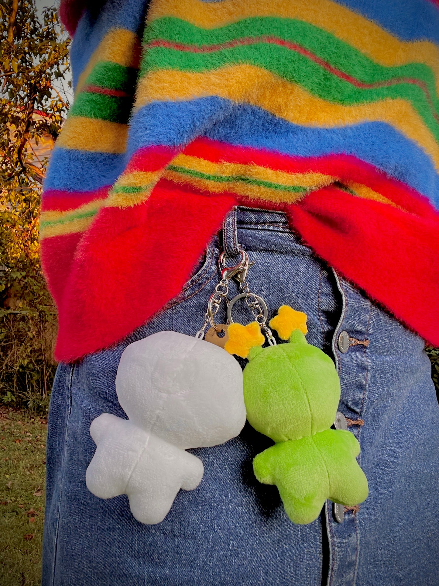 Colorful striped sweater with the back of a white plush and a green plush keychains attached to a person's jean skirt.