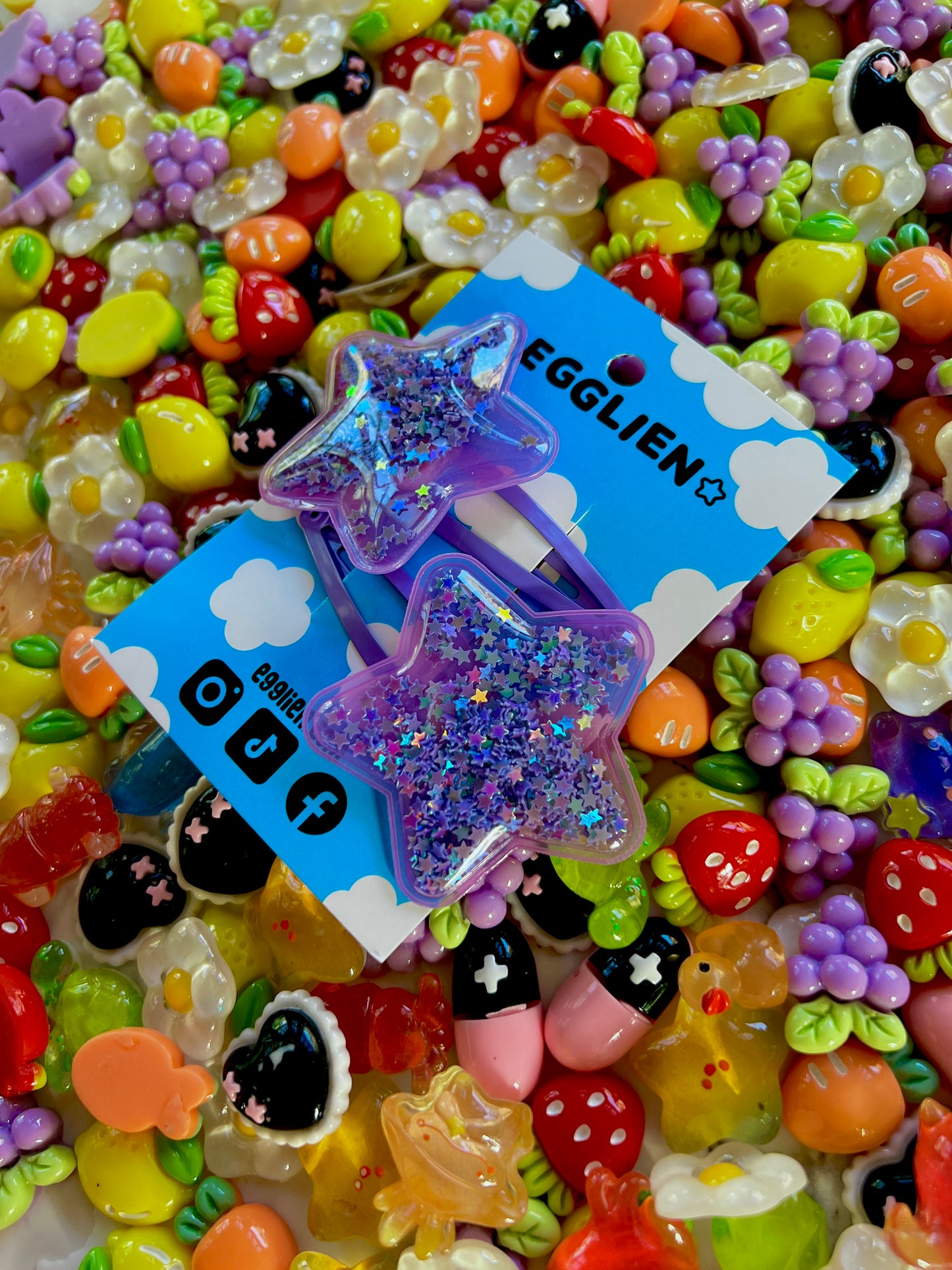 Two purple pvc stars filled with star glitter hair clips on a blue card with 'EGGLIEN' branding, surrounded by colorful decorative resin pieces