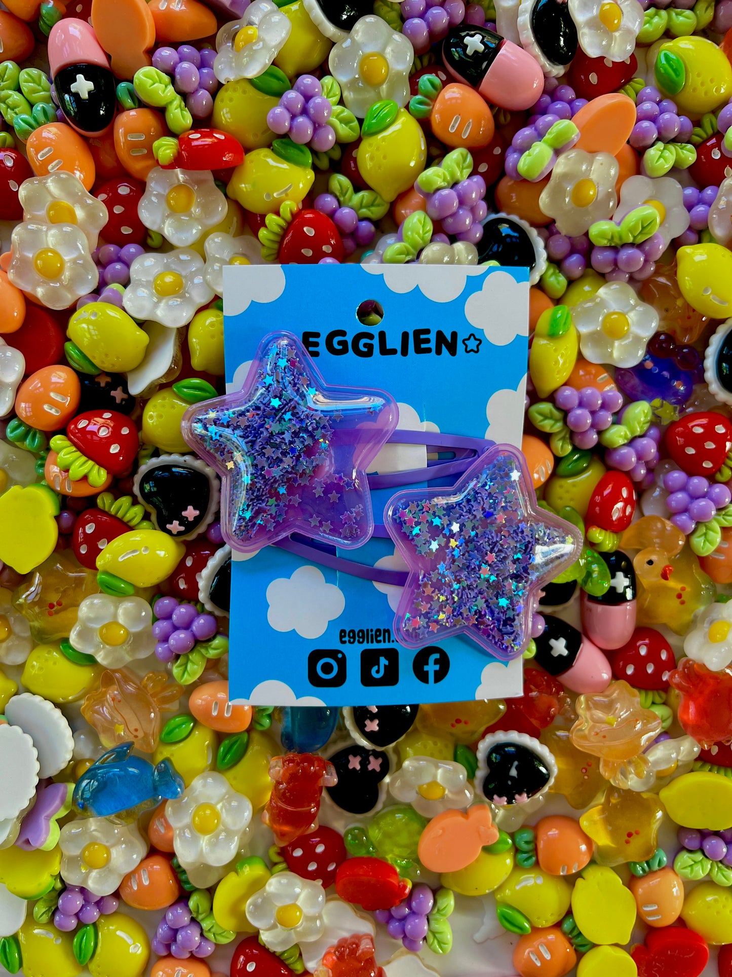 Two purple pvc stars filled with star glitter hair clips on a blue card with 'EGGLIEN' branding, surrounded by colorful decorative resin pieces