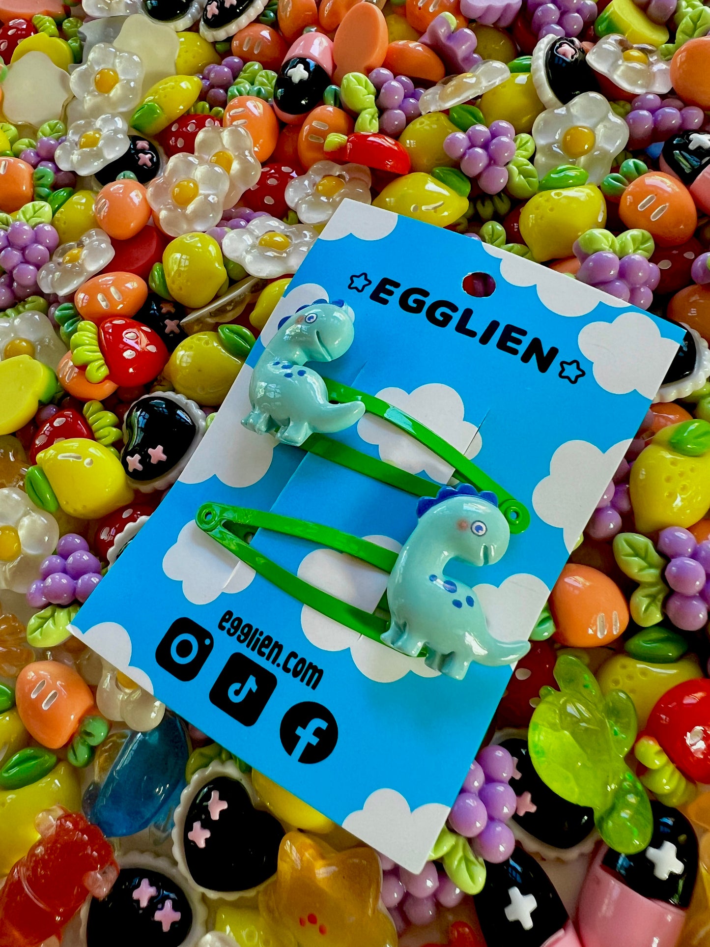 Colorful resin charms with dinosaur design on a blue Egglien card against a vibrant background
