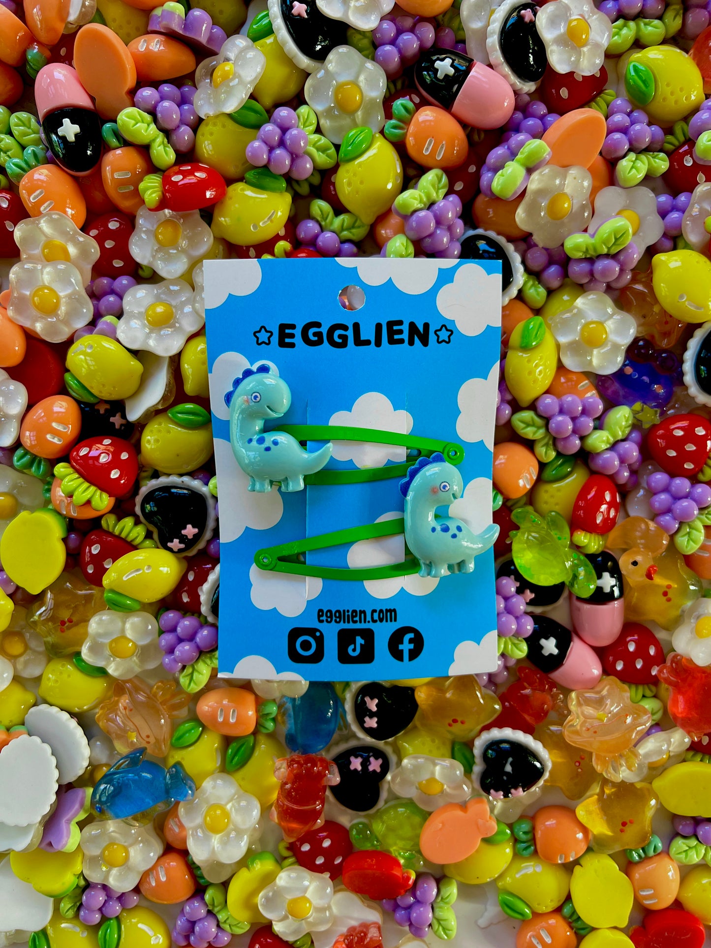 Colorful resin charms with dinosaur design on a blue Egglien card against a vibrant background