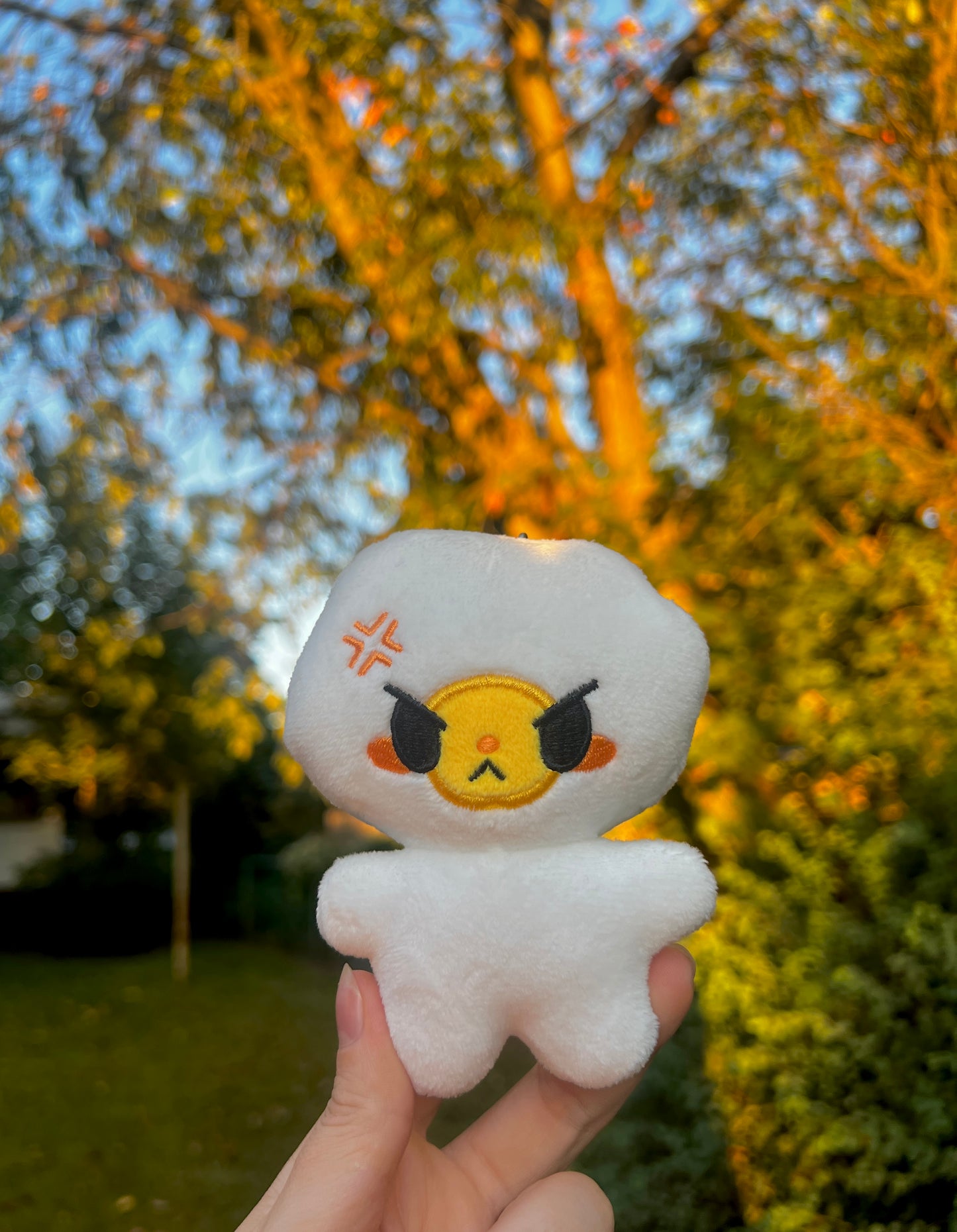White egg plush with an angry face held in front of a blurred outdoor background with trees.