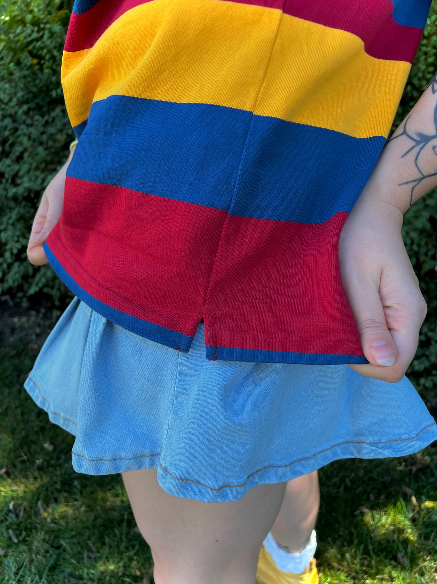 Girl wearing a red, yellow and blue shirt outdoors showing the side seam and slit of the shirt