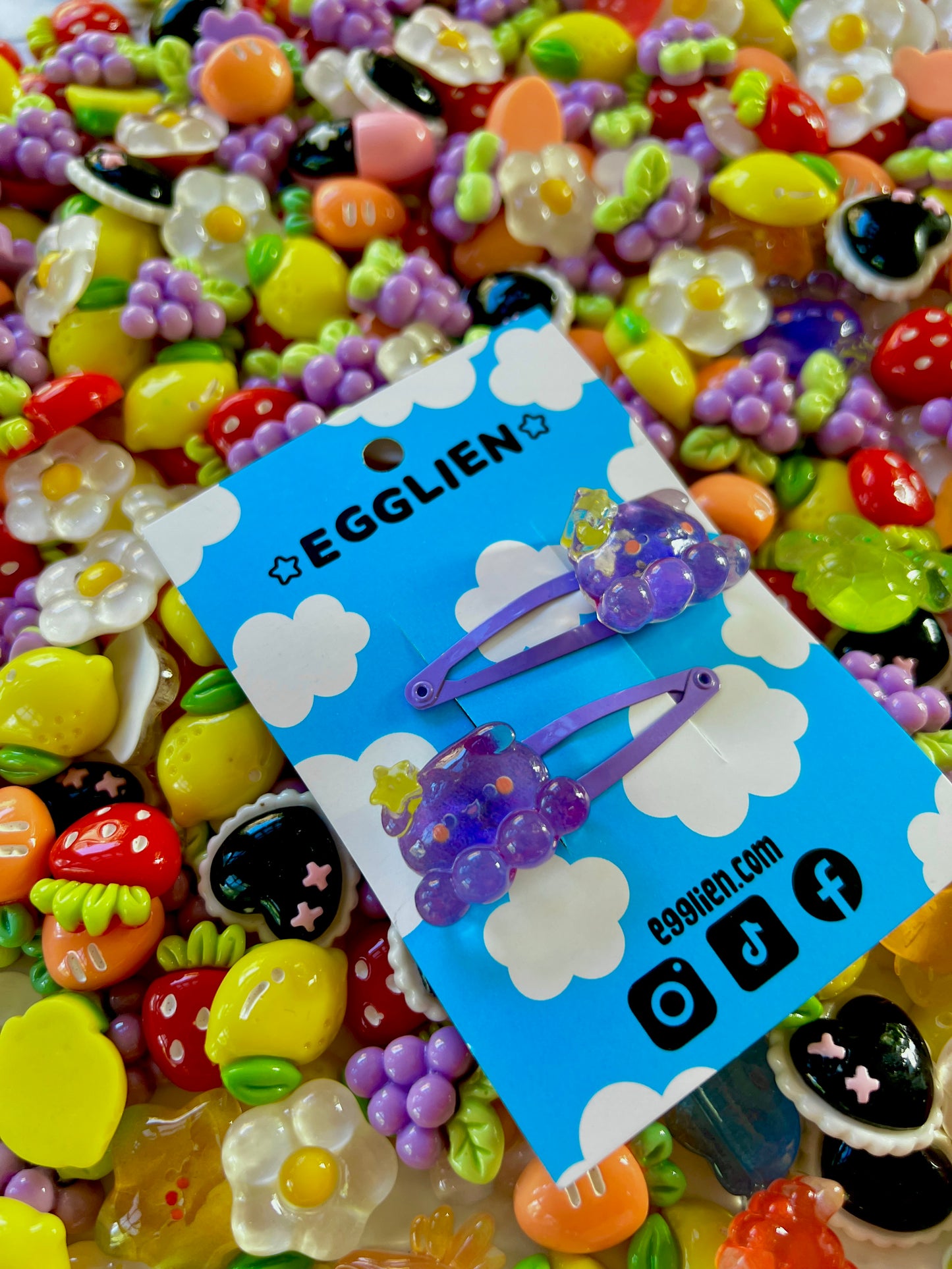 Two purple octopus with a yellow star hair clips on a blue card with 'EGGLIEN' branding, surrounded by colorful decorative resin pieces.
