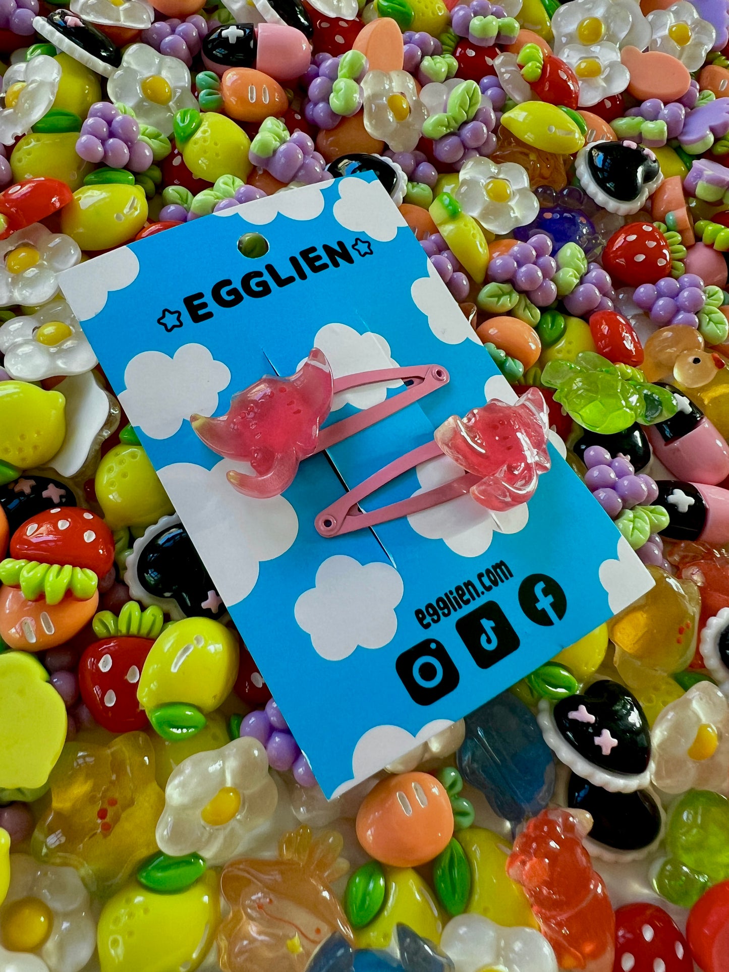 Two pink ray hair clips on a blue card with 'EGGLIEN' branding, surrounded by colorful decorative resin pieces