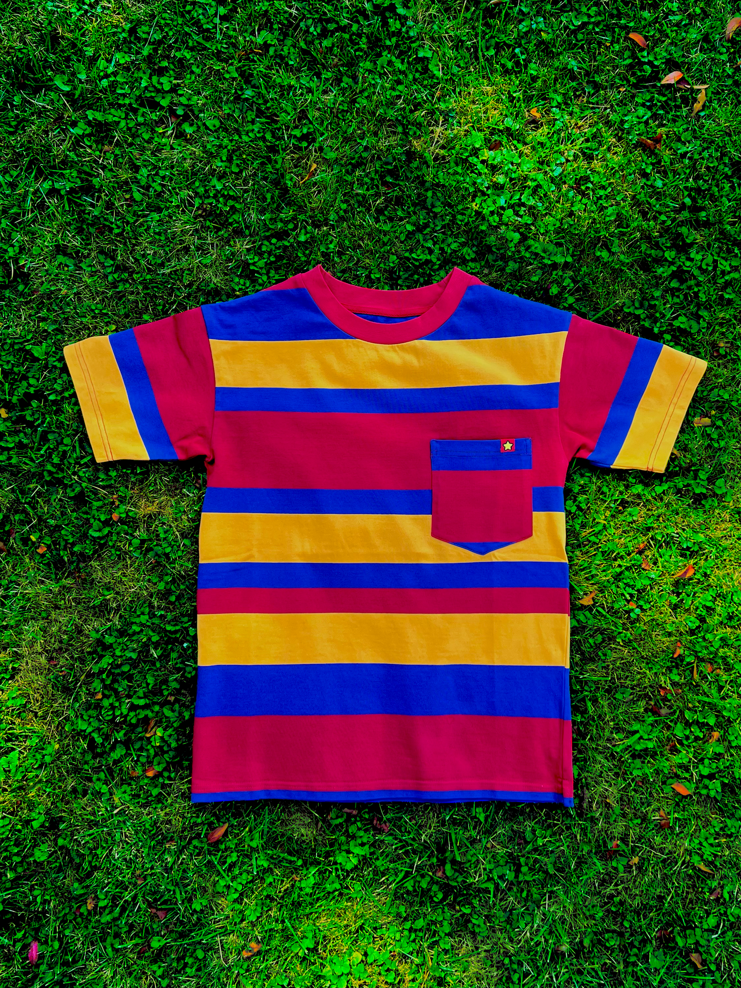 Red, yellow, blue striped shirt with mismatched stripes on the sleeves and pocket laying flat on grass