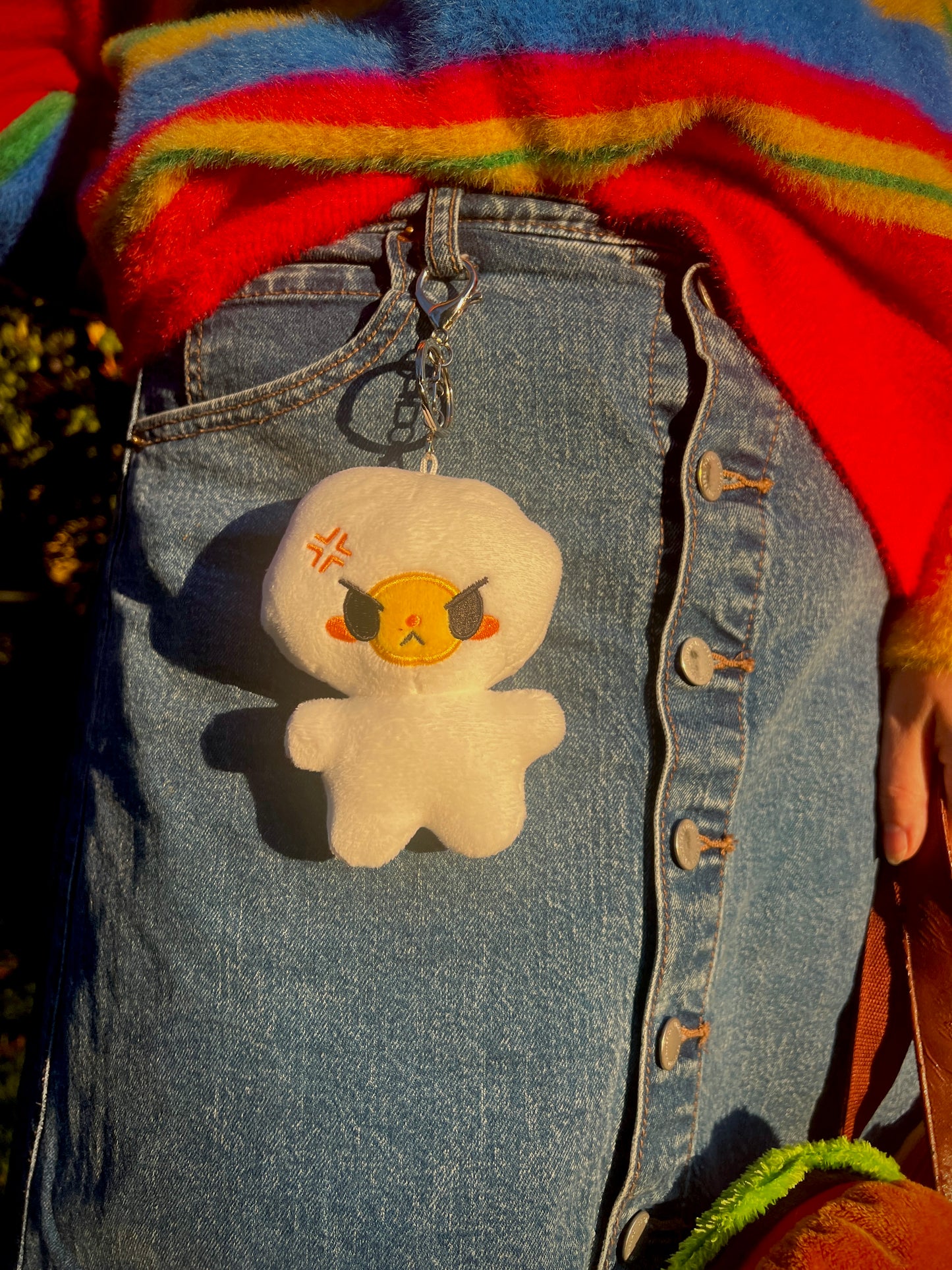 Plush egg keychain with angry expression hanging on a girl wearing aJean skirt and a rainbow sweater