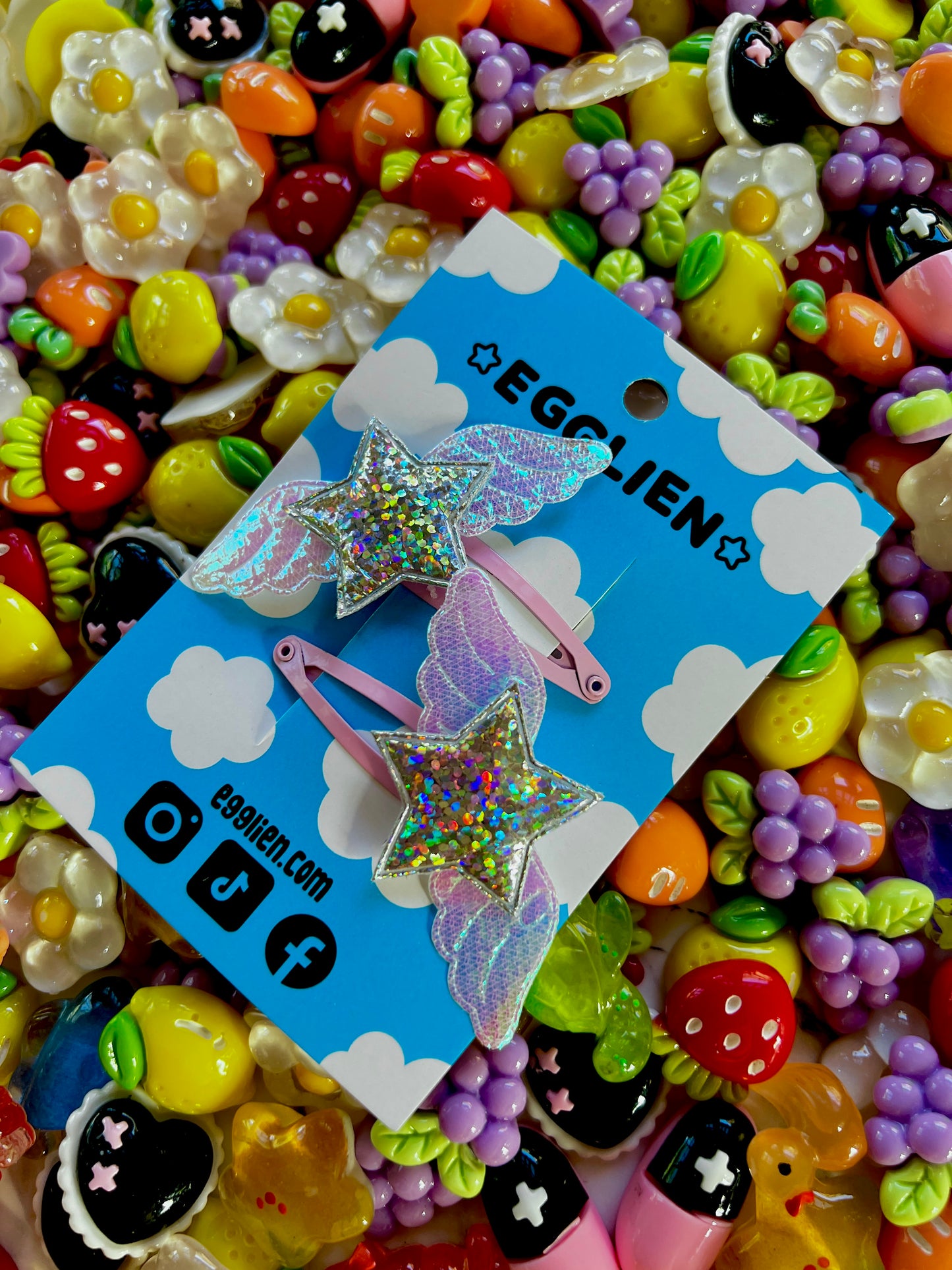Egglien Holographic silver star and holographic white wings on a pink hairclip with a background of colorful resin pieces