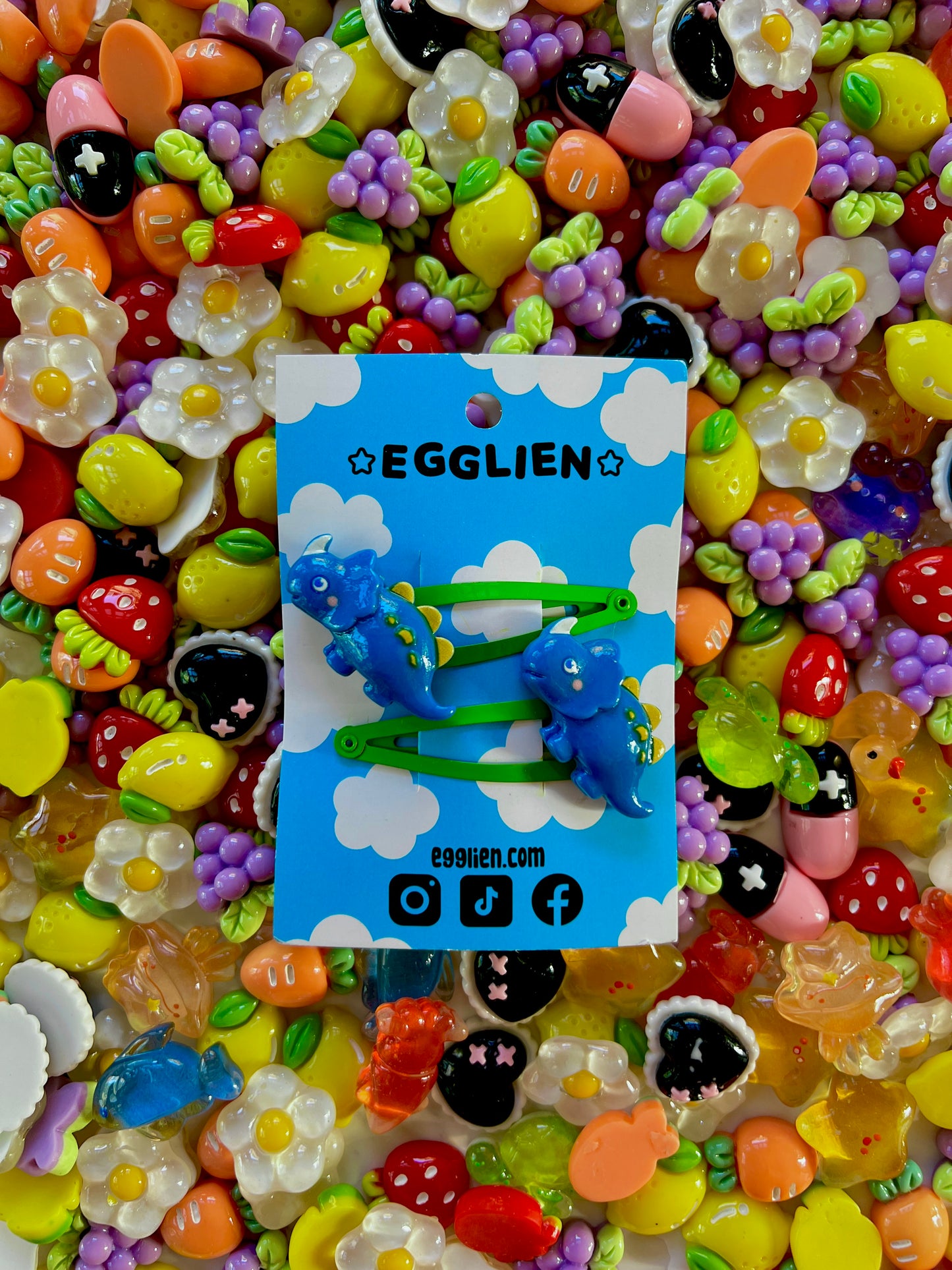 Dark Blue dinosaur-shaped hair clips on a blue card with 'EGGLIEN' branding, surrounded by colorful decorative resin pieces.