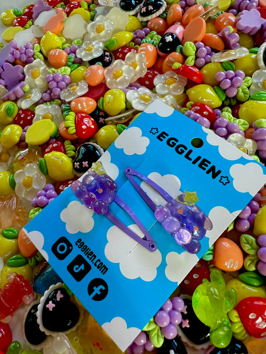 Two purple octopus  with a yellow star hair clips on a blue card with 'EGGLIEN' branding, surrounded by colorful decorative resin pieces.