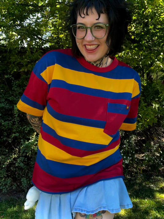 Person wearing a bright red ,yellow and blue striped shirt with a jean skirt outdoors.