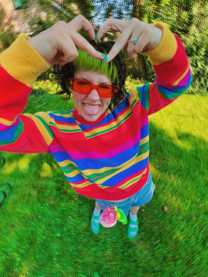 Person wearing a Rainbow striped sweater and red sunglasses outdoors on grass