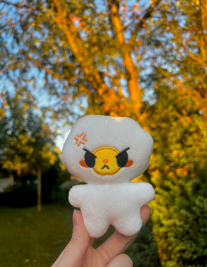 White egg plush with an angry face held in front of a blurred outdoor background with trees.