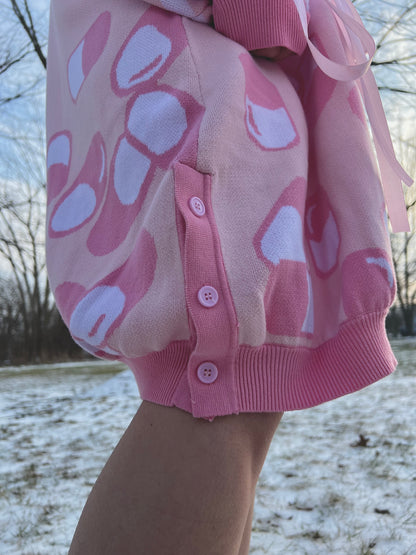 Girl is standing in the snow while wearing the menhera cardigan. It is a close up picture showing one of the side seam slits that has three light pink buttons. 