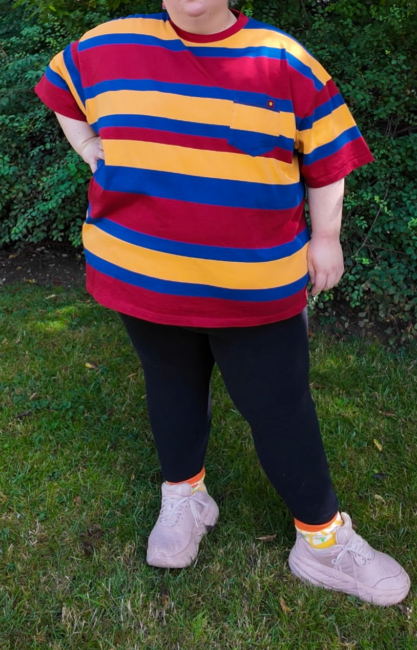Girl standing outside on grass wearing a red, blue and yellow striped shirt, black leggings, and white shoes 