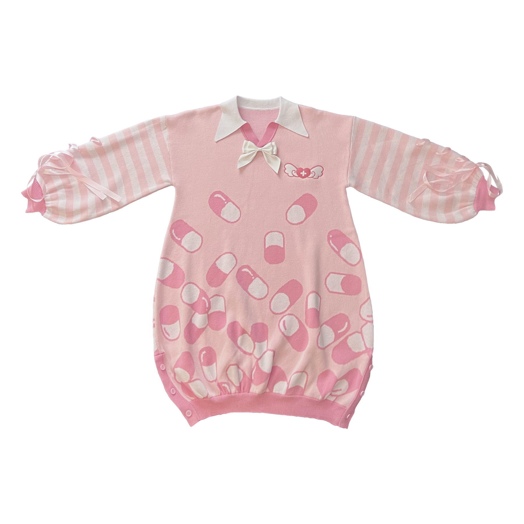 Flat lay image of the front of the pink menhera sweater dress. The sweater dress body is pastel pink with darker pink and white capsules on it. It has a white pointed collar and a removable white ribbon on the center collar. The sleeves are pastel pink and white striped with pastel pink ribbons installed to form a bow on the end of the sleeves. There is a darker pink and white embroidered heart with a cross and wings on the front left chest.
