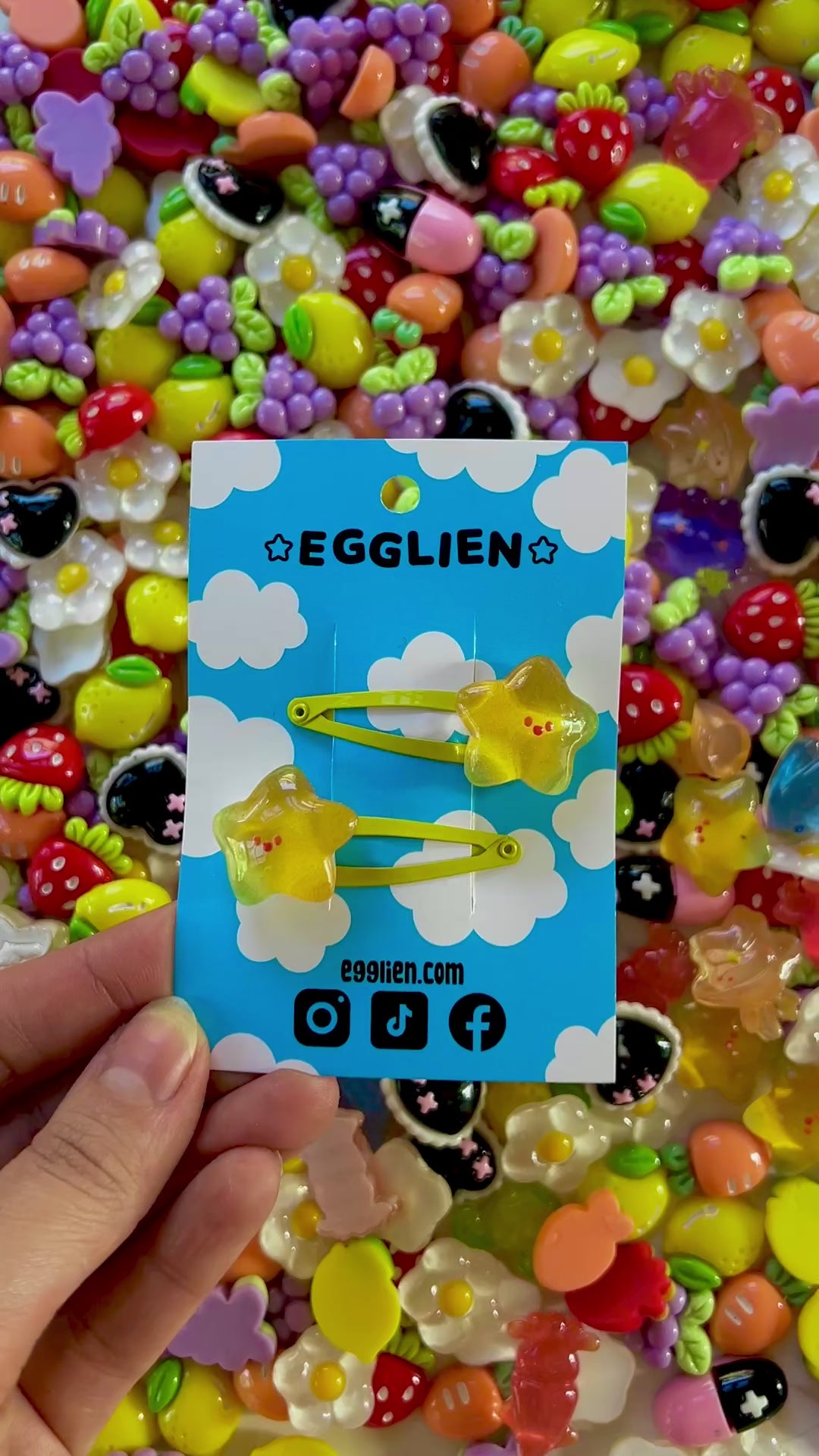 Two yellow star with happy faces hair clips on a blue card with 'EGGLIEN' branding, surrounded by colorful decorative resin pieces