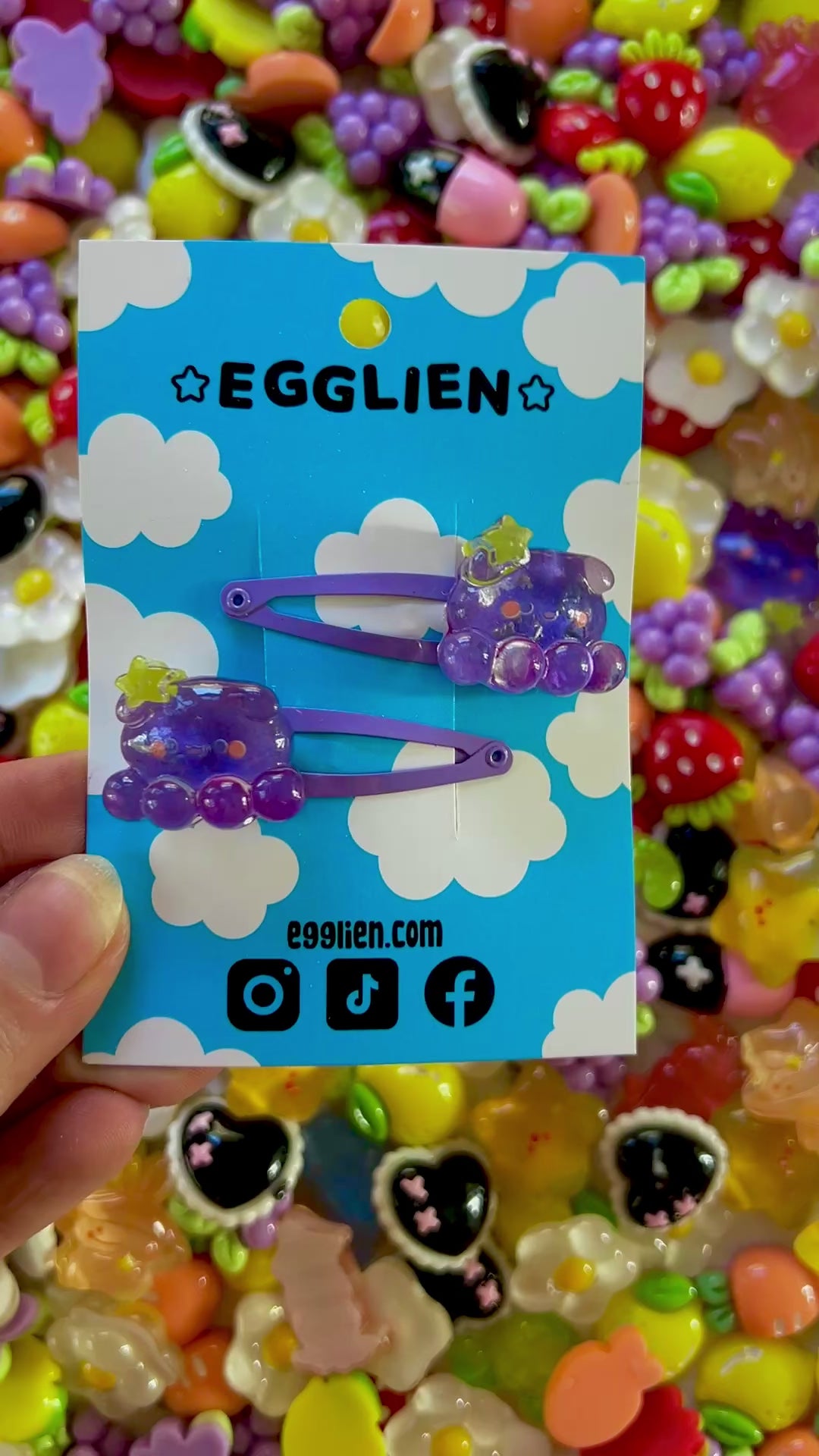 Two purple octopus  with a yellow star hair clips on a blue card with 'EGGLIEN' branding, surrounded by colorful decorative resin pieces.