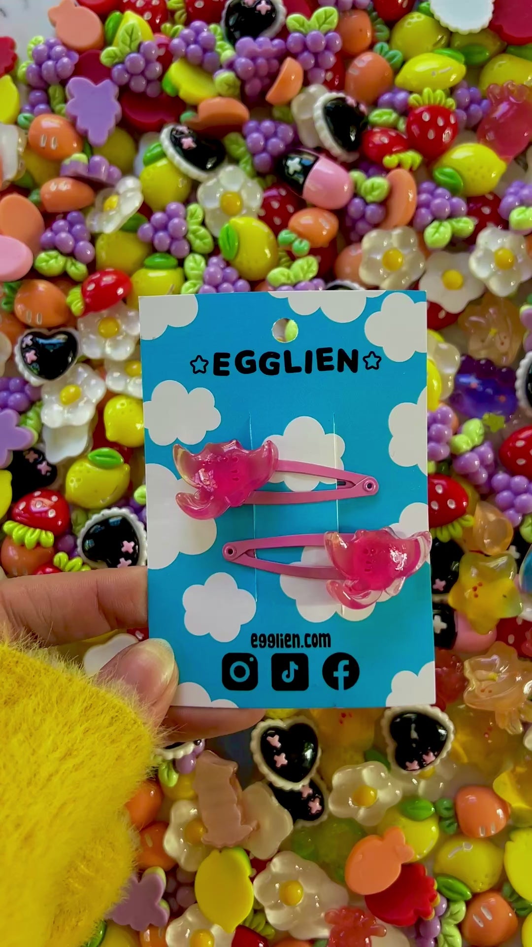 Two pink ray hair clips on a blue card with 'EGGLIEN' branding, surrounded by colorful decorative resin pieces