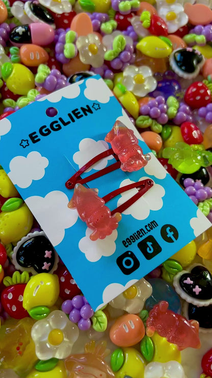 Two red squid hair clips on a blue card with 'EGGLIEN' branding, surrounded by colorful decorative resin pieces