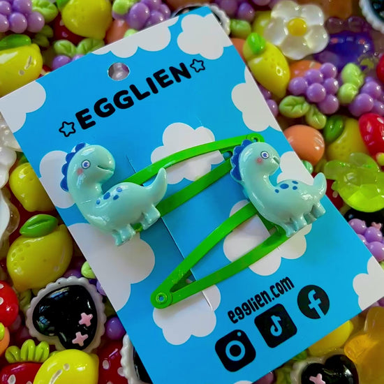 Colorful resin charms with dinosaur design on a blue Egglien card against a vibrant background