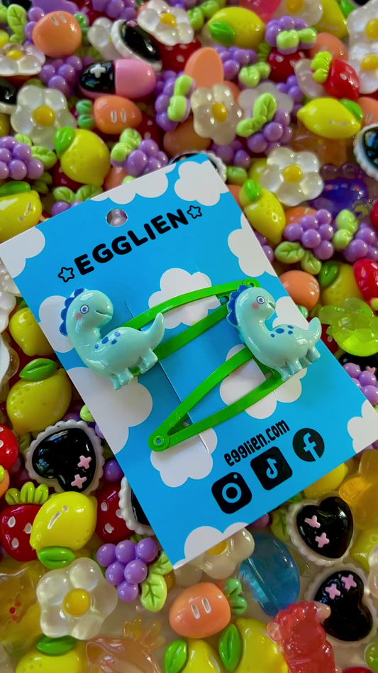Colorful resin charms with dinosaur design on a blue Egglien card against a vibrant background