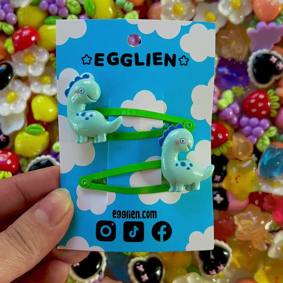 Colorful resin charms with dinosaur design on a blue Egglien card against a vibrant background