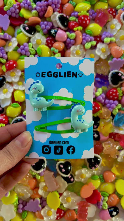 Colorful resin charms with dinosaur design on a blue Egglien card against a vibrant background