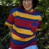 Person wearing a bright red ,yellow and blue striped shirt with a jean skirt outdoors.