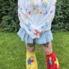 Woman standing outside wearing a white crew neck with clown themed characters, a denim skirt, and knee-high legwarmers with star patterns.