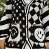 A black and white cardigan with a geometric pattern featuring stars and smiley faces, displayed on a girl facing the camera