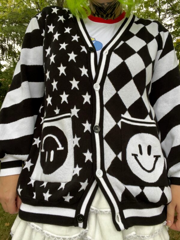 A black and white cardigan with a geometric pattern featuring stars and smiley faces, displayed on a girl facing the camera