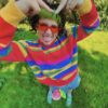 Person wearing a Rainbow striped sweater and red sunglasses outdoors on grass