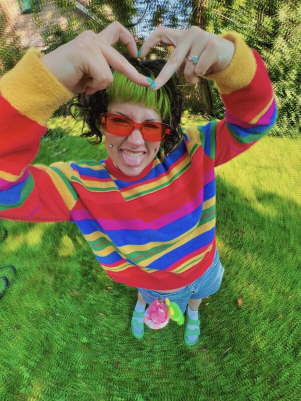 Person wearing a Rainbow striped sweater and red sunglasses outdoors on grass