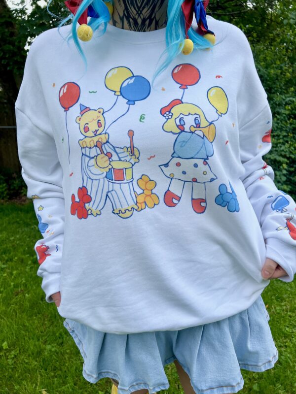 Woman wearing a white sweatshirt with colorful clown design and a jean skirt outdoors.