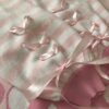The pastel pink and white sleeves of a knit cardigan are shown close up. Showcasing the darker pink cuffs along with the pastel pink ribbons that are installed in each of the sleeves. The ribbon is shaped in three hearts that get closer to the cuffs where they combine to create a big pastel pink bow.
