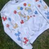 White sweatshirt with clown graphics laying flat on grass