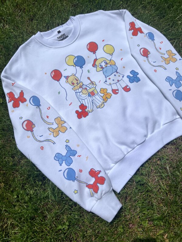 White sweatshirt with clown graphics laying flat on grass