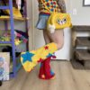 Woman with her body facing the side with one leg in the air. She is wearing a diagonal checkered vest, jean skirt, yellow dog bag and colorful star legwarmers.