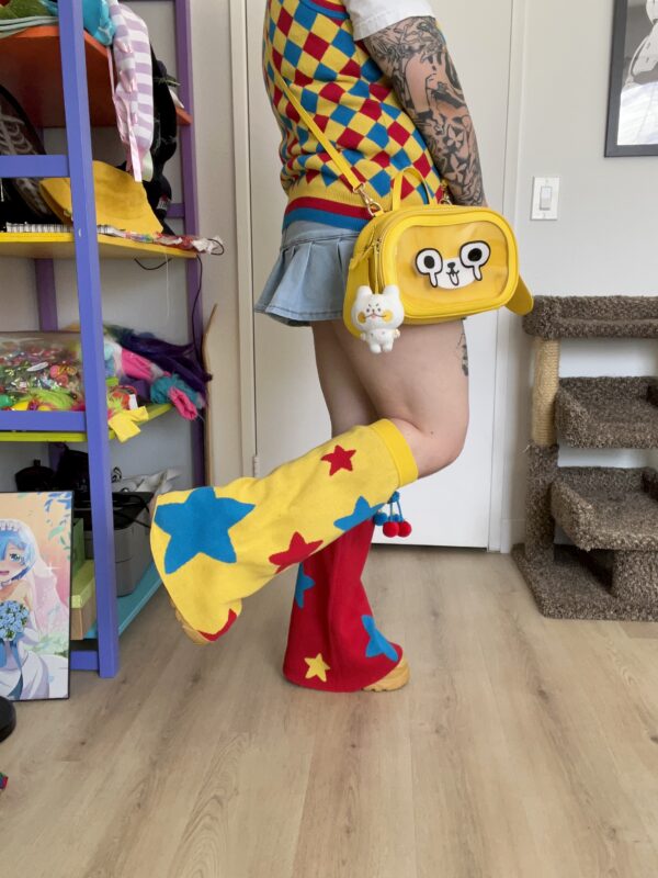 Woman with her body facing the side with one leg in the air. She is wearing a diagonal checkered vest, jean skirt, yellow dog bag and colorful star legwarmers.