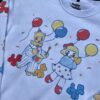 Close up photo of a white crew neck with clown and balloon graphics laying on grass