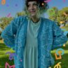 A person standing on grass wearing a blue cardigan with a geometric water pattern, paired with a lighter blue dress. There are colorful confetti-like shapes overlaid on the image.