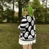 Girl standing in a green field with back facing the camera wearing a black and white happy face cardigan and a white skirt.