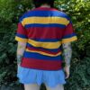 Person wearing a red, yellow, and blue striped shirt with a blue skirt outdoors with back facing the camera showing the back of the shirt