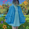 A person standing on grass wearing a blue cardigan with a geometric water pattern, paired with a lighter blue dress. There are colorful confetti-like shapes overlaid on the image.