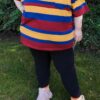 Girl standing outside on grass wearing a red, blue and yellow striped shirt, black leggings, and white shoes