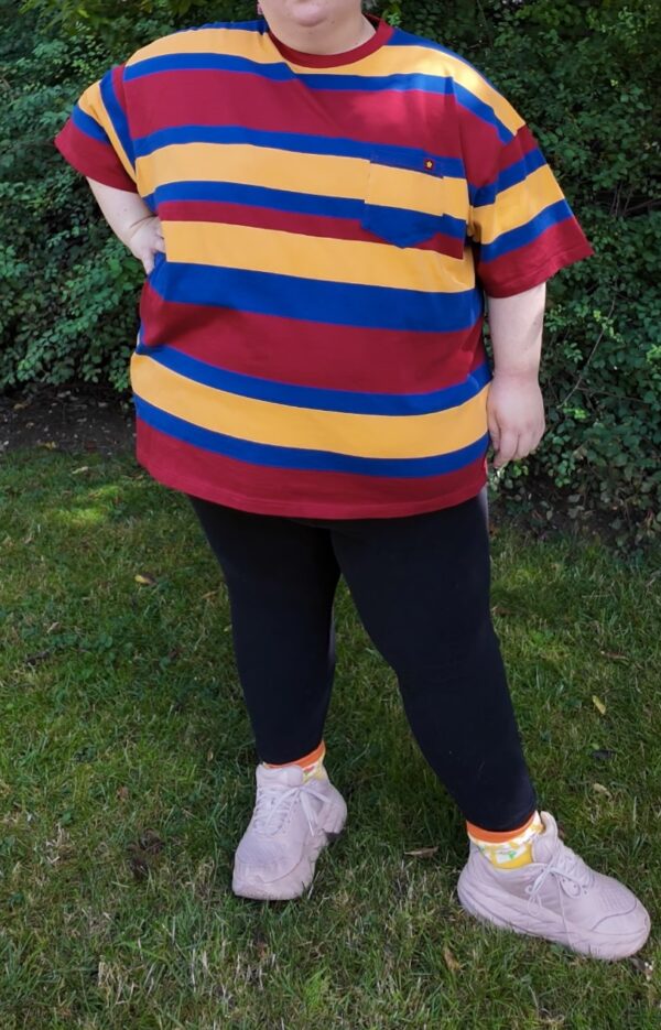 Girl standing outside on grass wearing a red, blue and yellow striped shirt, black leggings, and white shoes