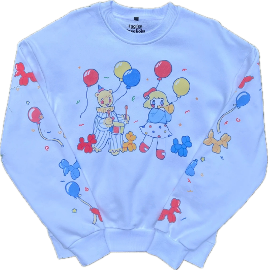 A white crew neck with colorful clown and balloon themed graphics printed on the front and on the sleeves laying flat on a clear background