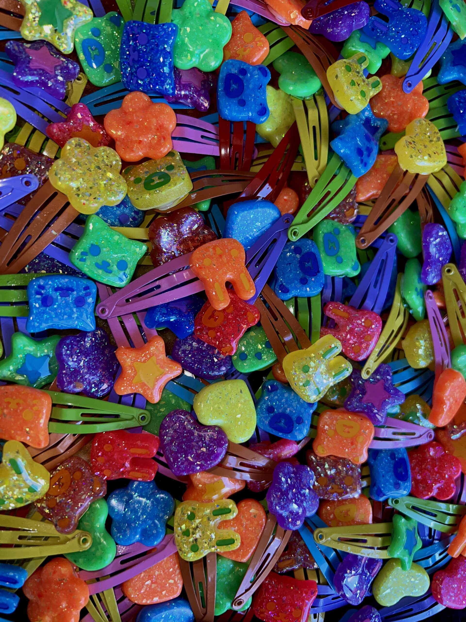 A large overview picture of many colorful resin hairclips in a variety of colors and shapes including bunny, heart, bear, cat and star.