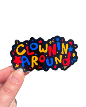 A hand holding a sticker with the text 'CLOWNS AROUND' in a colorful font